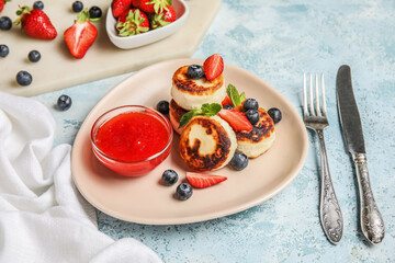 Plate with cottage cheese pancakes, berries and strawberry jam on blue background