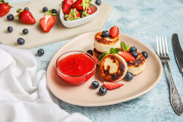 Plate with cottage cheese pancakes, berries and strawberry jam on blue background
