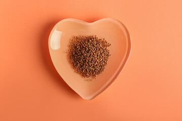 Heart shaped plate with buckwheat grains on color background