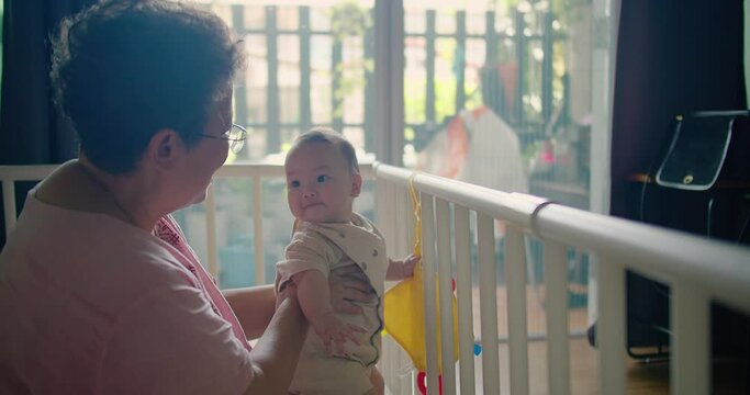 happy senior Asian woman grandmother teaching holding her granddaughter baby learning to stand takes first steps at home, Two age generations family old grandparent enjoying activity together