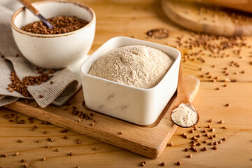 Board with bowls of flour and buckwheat grains on wooden background