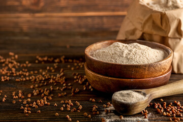 Bowl of flour, spoon and buckwheat grains on dark wooden background