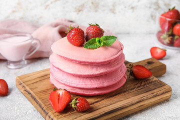 Wooden board with tasty pink pancakes and strawberry on light background