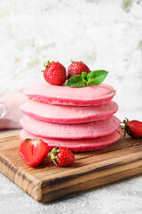 Wooden board with tasty pink pancakes and strawberry on light background, closeup