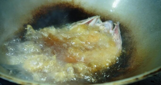 Deep frying fresh Sea Bass barramundi fish in frying pan with hot bubbles oil at the kitchen, preparing cooking thai food