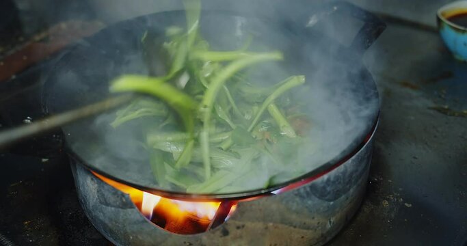 Close up chef cooking stir frying vegetable fresh green Spicy water spinach with fire flame at the kitchen , Thai food, fresh morning glory with red chili and garlic