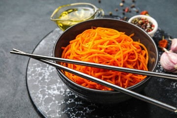 Bowl of tasty korean carrot salad and chopsticks on dark background, closeup