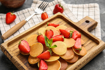 Wooden board with tasty mini pancakes and strawberry on table