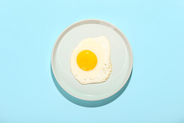 Plate with fried egg on blue background