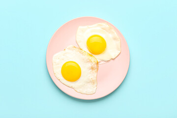 Plate with tasty fried egg on blue background
