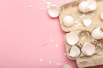 Cardboard holder with broken egg shells on pink background, closeup