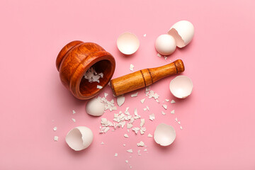 Wooden mortar and pestle with broken egg shells on pink background