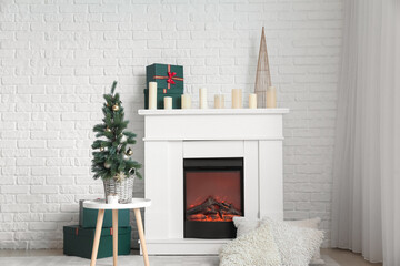Electric fireplace with candles, gift boxes and Christmas tree near white brick wall