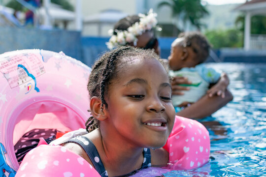 Cute little girl having fun at the pool. Mother and son in the background. Goofy face
