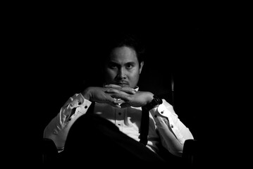 Asian Mafia boss sitting in a chair with a black background.