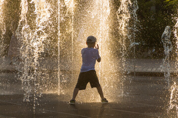 Uralsk, Kazakhstan (Qazaqstan), 8.07.2022 - The boy plays on the dancing fountain. Fountain from the floor on a hot day. Dry fountain in the city park.