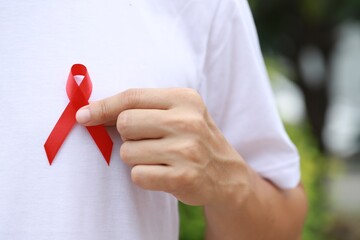 Due in December world aids day and Lymphoma Awareness Day National Red Ribbon Week health care concept and world cancer day man holding red ribbon Closeup with space for text