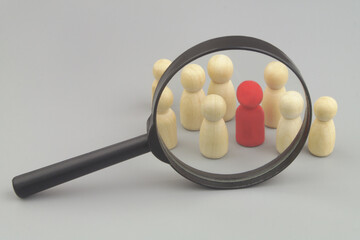 Wooden people figures under magnifying glass, one figure is red as employer with skills. Hire workers and find talents concept.