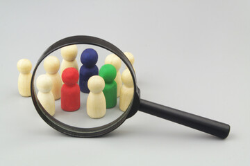 Group of not colored figures with  few colored under magnifying glass on grey background. Choosing personnel and hire employers, HR and people recognition concept.