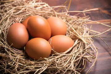 fresh chicken eggs in straw on wooden background