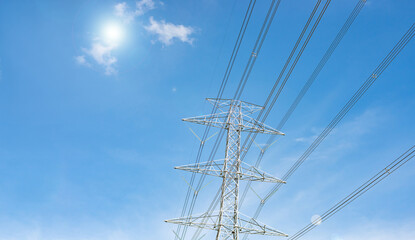 High-voltage poles and power lines contrast with the blue sky and clouds. bottom view of electric...