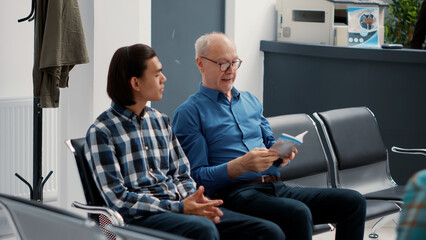 Diverse group of patients sitting on chairs in waiting room lobby at hospital reception, waiting to be called at medical appointment. People with healthcare insurance in clinic waiting area.
