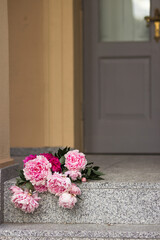 Bouquet of pink gardening peonies lies on steps near the old grey wooden door.