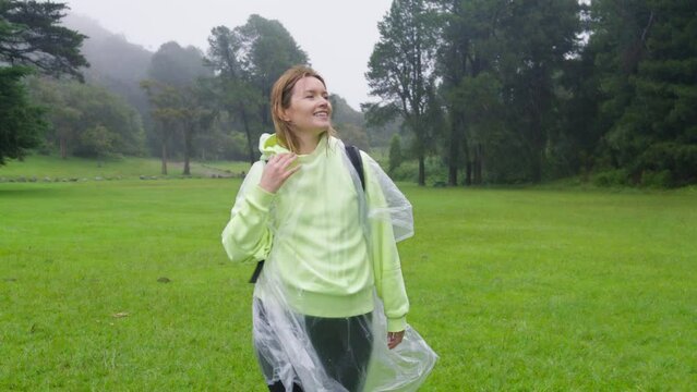 Happy woman smiles under tropical rain. Free carefree woman with raised arms enjoying nature under rain in slow motion. Concept of love, nature, happiness, freedom. Traveler on hike in green forest