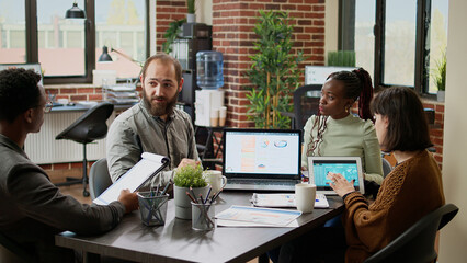 Diverse team of business people working on research report, doing collaboration meeting in boardroom office. Coworkers brainstorming ideas and analyzing project charts, networking data.