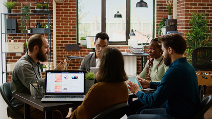 Diverse team of business people working on partnership report, analyzing charts on documents to plan presentation. Coworkers looking at management data on papers and digital tablet.