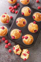 Summer raspberry muffins with white chocolate close-up in a muffin pan on the table. Vertical top view from above