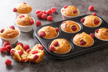 Baked raspberry muffins with white chocolate and fresh berries close-up in a muffin pan on the table. Horizontal