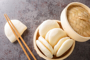 Chinese steamed buns Gua bao in a bamboo steamer close-up on the table. horizontal top view from...