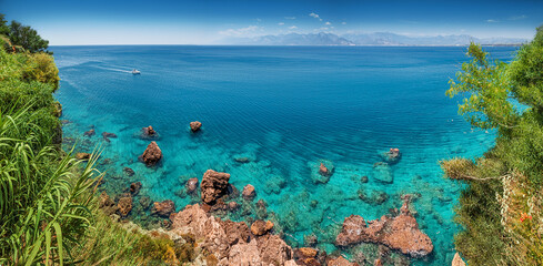 Aerial scenic panoramic seascape view from a high cliff. Vacation background and coastline concept. Azure sea bottom and sailing motor boat on a transparent waters