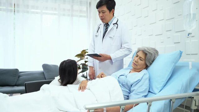 Male doctor came to report the symptoms of an elderly female patient. let her daughter listen while an elderly female patient was sleeping on a bed in the hospital room. Patient's daughter learned.