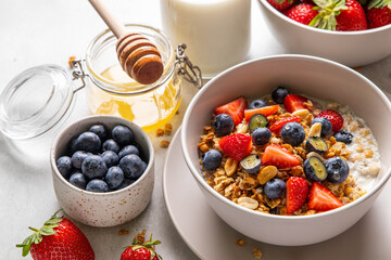 Homemade granola with yogurt or milk, blueberry, strawberry and honey in bowl on grey background. Healthy breakfast. Selective focus.