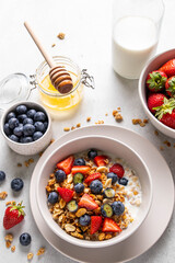 Homemade granola with yogurt or milk, blueberry, strawberry and honey in bowl on grey background. Healthy breakfast. Selective focus.