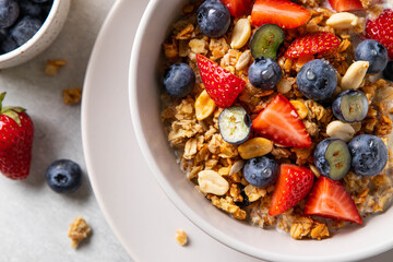 Homemade granola with yogurt or milk, blueberry, strawberry and honey in bowl on grey background. Healthy breakfast. Selective focus.