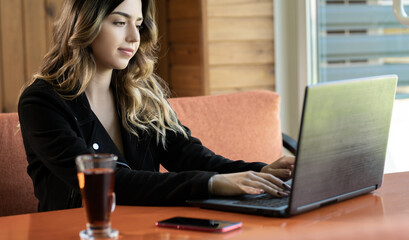 Beautiful brunette using laptop in cafe, young female freelancer using laptop computer for distance work while sitting in co-working cafe