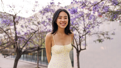 Happy young chinese woman look with smile at camera . Fair-skinned pretty lady staying in park wearing yellow dress. Lifestyle concept 