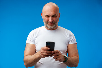 Happy middle-aged man with a phone in his hands against blue background