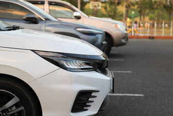 Closeup of front side of white car with other cars parking in outdoor parking area. in twilight evening.