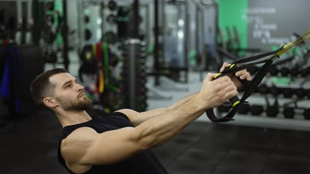 Side view of strong sportsman doing exercises with TRX straps at gym