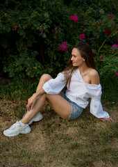 beautiful brunette girl  in white embroidered shirt  in the garden with pink roses flowers	