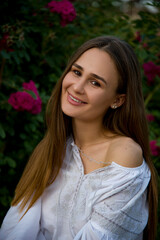 beautiful brunette girl in white embroidered shirt in the garden with pink roses flowers