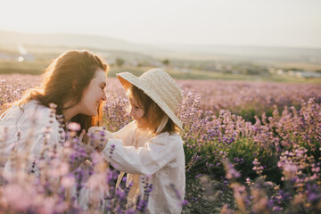 Happy mother and daughter wearing white vintage dresses having fun in lavender field at sunset.