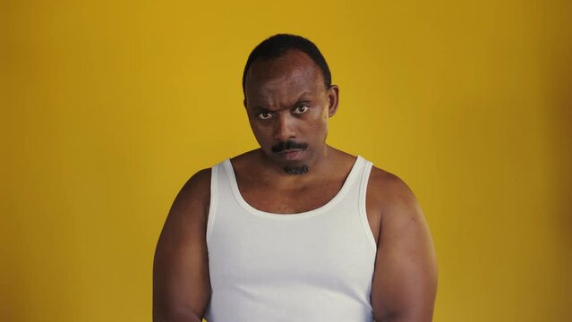 African man standing on a yellow background.Man plays with his muscles on camera. Squeezes his pecs and looks at the camera. Black man playing on camera.