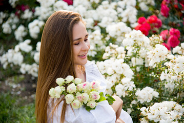 Naklejka premium portrait of a beautiful brunette smiling woman in white embroidered shirt and jeans shorts with bouquet of white roses flowers in summer park