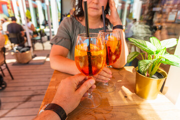 Two cocktail glasses in the middle age man and woman hands in a outdoors cafe.Summer vacation concept.Closeup.
