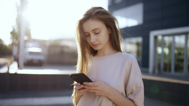 Young woman in a bright sunlight uses phone